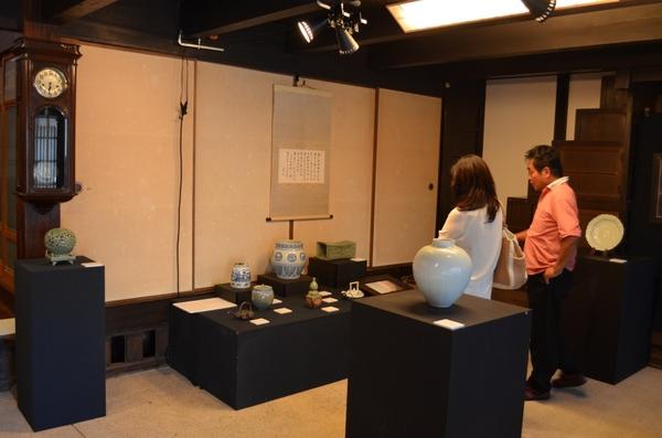 奥にある黒い棚に壺や急須などが並べられていてそれを2人の男女が見ている写真